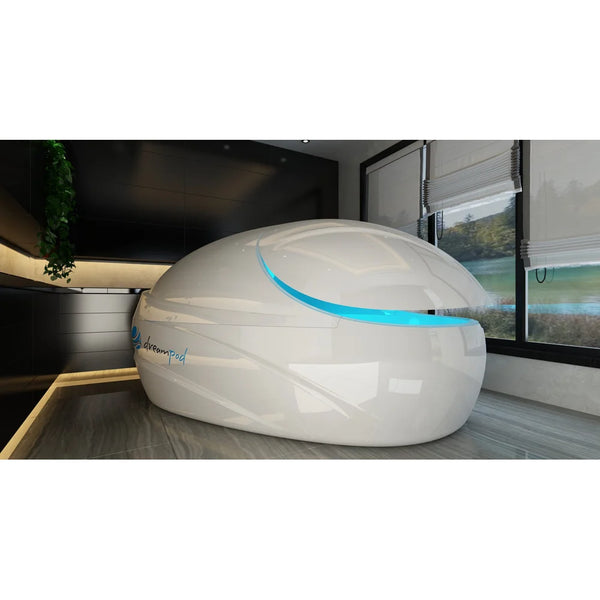 Glossy white pod with closed lid and blue lit door seam beside a window, the Dreampod Vmax Float Pod in a spa room