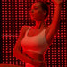 Woman in a white sports top poses before glowing red LED rows of the Kore KoreKapsule Near Infrared Light Therapy System